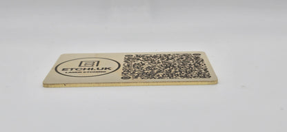 Rectangular brass business card with QR code and text on a white background