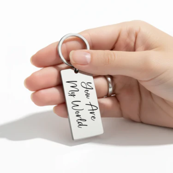 Hand holding a keychain with 'You Are My World' text on a white background