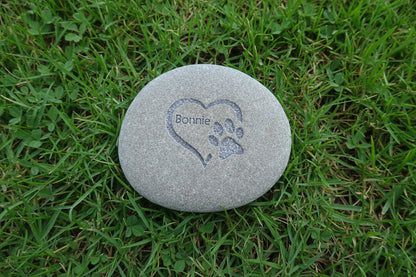 Round stone with engraved heart and paw print on a grass surface